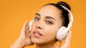 A young woman wearing headphones and enjoying music against an orange background in a studio setting.